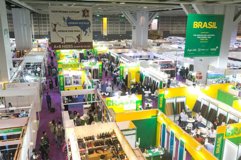 Blick von oben auf eine Ledermesse mit bunten Messeständen in Gelb, Grün und Lila, zahlreichen Besuchern und Ausstellern in einer großen Messehalle.