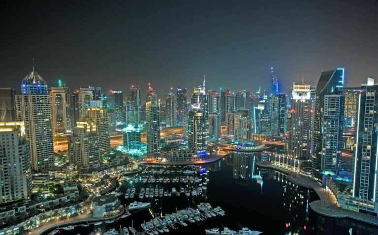 Nächtliche Skyline von Dubai mit beleuchteten Hochhäusern und Jachthafen am Wasser