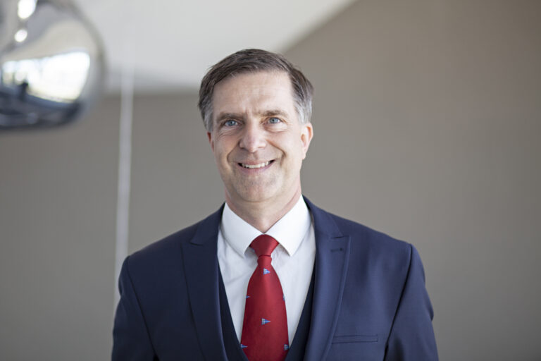 Porträt von Dr. Christoph Riemer im dunkelblauen Anzug und roter Krawatte