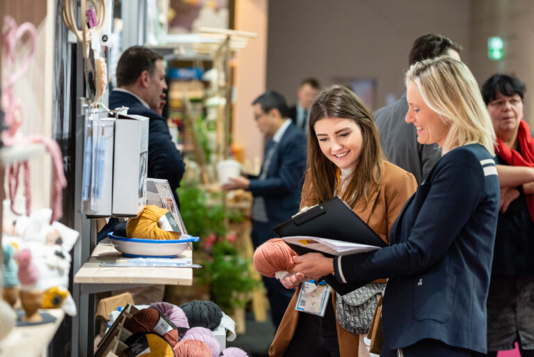 Zwei Frauen besichtigen eine Ausstellungsfläche mit Lederprodukten und Accessoires auf einer Fachmesse.