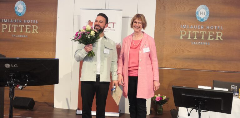 Elias Sattler erhält Blumenstrauß von Frau in rosa Jacke bei VGCT-Förderpreisverleihung im Imlauer Hotel Pitter Salzburg.