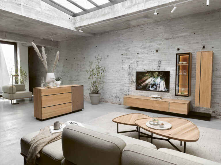 Modernes Wohnzimmer mit Holzmöbeln, grauer Polstercouch, Couchtisch und TV-Wandschrank vor Backsteinwand mit Oberlichtern.
