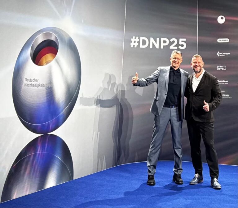 Zwei Männer stehen auf blauer Bühne vor großem silbernem Ei-Objekt mit deutscher Flagge und #DNP25 Hashtag.