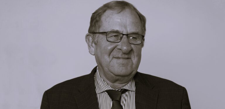 Porträt eines älteren Mannes mit Brille und Anzug vor neutralem Hintergrund