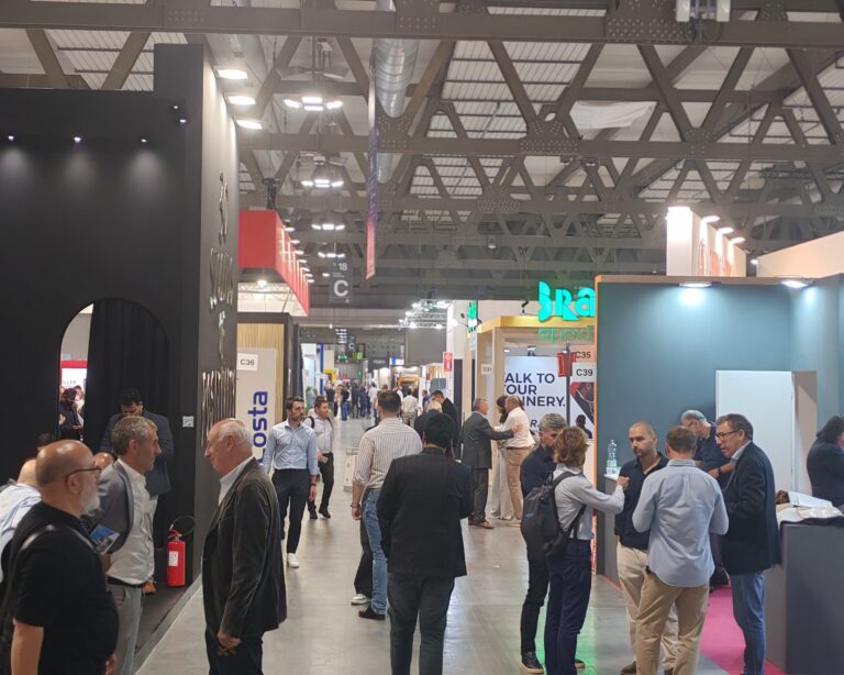 Besucher auf einer Fachmesse in einer großen Industriehalle mit Ausstellungsständen und Messebuden.