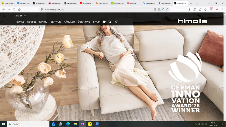 Frau sitzt entspannt auf cremefarbenem Polstersofa mit Blumenvase und Kissen im modernen Wohnzimmer